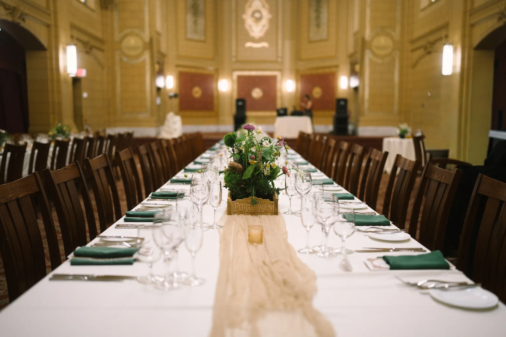 Completed wedding table with custom floral centerpiece boxes, green napkins, and a wood table runner